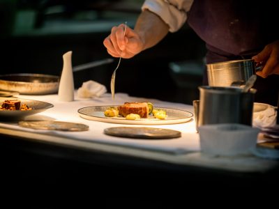 Chef preparing a dish with meat on a plate under a light. The ch
